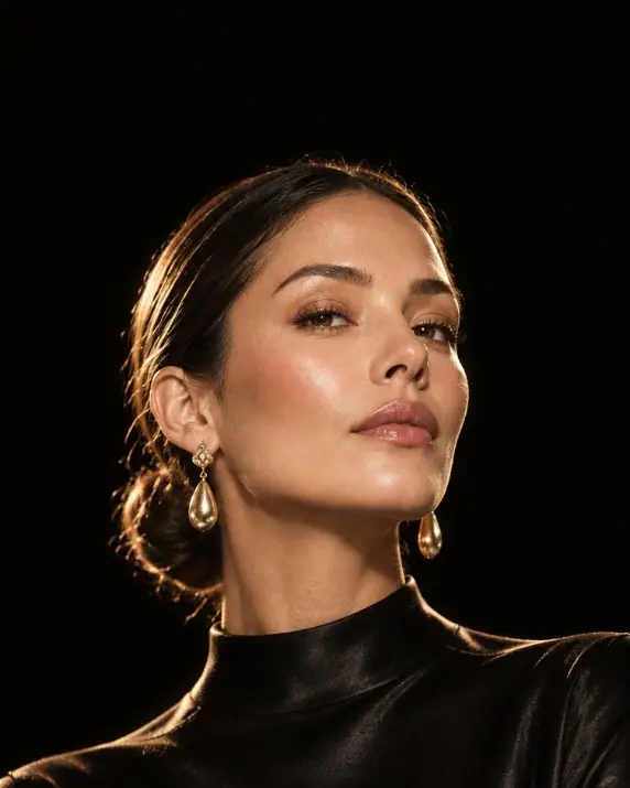 Woman in a black silk top, looking upward in warm light.